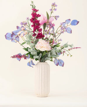 A white textured vase showcases the "Silk Artificial Flowers Bouquet Amethyst Romance" with pink peonies, purple and blue flowers, burgundy flowers and green foliage against a light, neutral background.