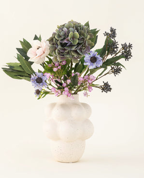 The Blue Belle silk artificial flower bouquet - with hydrangeas, daisies, pink roses and more - stands in a white structured vase against a plain light background.
