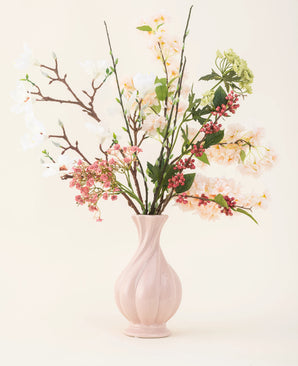 A pink ceramic vase contains the Springtime Poem silk artificial flower bouquet, with white, pink and green flowers with green leaves and brown stems, against a light background.