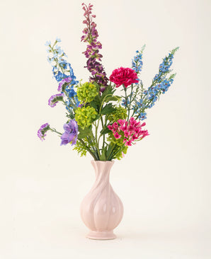 Arranged in a pink ceramic vase, the Blossom Breeze silk artificial flower bouquet features vibrant blue, purple, red and green flowers - a maintenance-free floral bouquet against a plain light background.