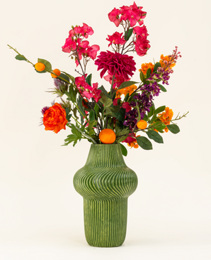 The Silk artificial flower bouquet Fiesta Sunset is arranged in a green textured vase and shows pink, orange and purple flowers with green leaves and small orange fruits against a light background.