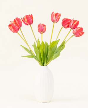 The Silk artificial flower bouquet French Tulip red is arranged in a white ceramic vase, with eight red and yellow tulips with green leaves against a plain light background.