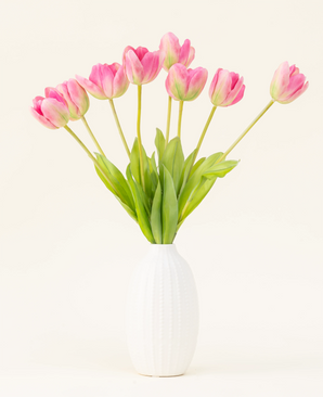 The Silk artificial flower bouquet French Tulip pink is arranged in a white vase, with pink French tulips and green leaves against a simple light background.