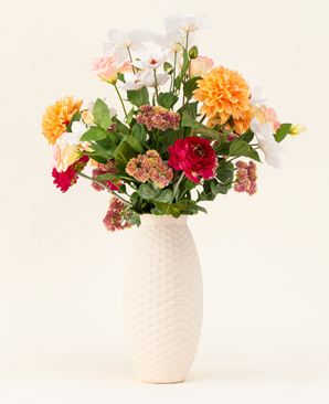 The Silk artificial flower bouquet The Wild Bunch, with red roses, Real Touch Dahlia, pink flowers and green leaves in a white structured vase, is shown against a light background.