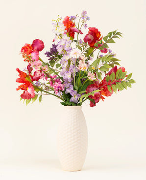 The Pink Pop silk artificial flower bouquet is in a vase with a white structure, with lively artificial pink flowers and green leaves against a light background.