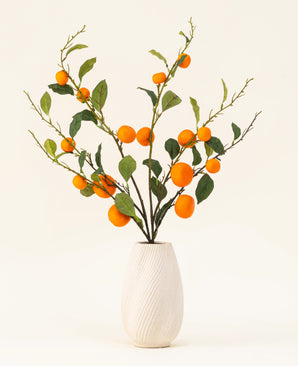 The Silk artificial flower bouquet Mandarin has a white textured vase and branches of green leaves and vibrant orange artificial mandarins, which add a lively touch against a plain light background.