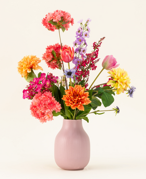 The Colourburst Blossom silk artificial flower bouquet has a pastel pink vase filled with orange dahlias, pink carnations, yellow dahlias, purple delphiniums and red tulips - ideal artificial bouquet decoration for any room.