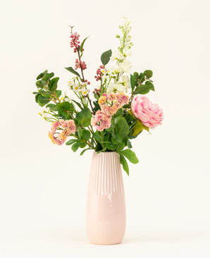 A pink ceramic vase displays the Daisy Charm silk artificial flower bouquet, with various flowers and greenery - pink roses, white blossoms and red berries - beautifully arranged against a plain light background.