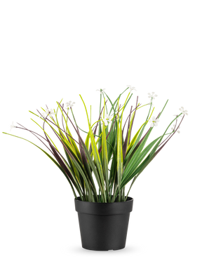 The Artificial Grass Plant in Pot UV 26 cm has long green and purple leaves with small white flowers, arranged in a simple black pot and displayed against a white background.