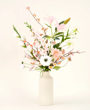 A cream-colored vase shows the Pink & Pearl silk artificial flower bouquet, with delicate pink, white and peach-colored silk flowers with green leaves against a light neutral background.