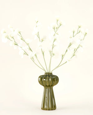A green ribbed glass vase holds the Silk artificial flower bouquet Pea cream with delicate white silk flowers and slender stems, against a plain off-white background.