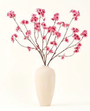 The Silk artificial flower bouquet Cherry blossom fuchsia 114 cm adds a vibrant pop of color to your interior with its striking branches and fuchsia blossoms, beautifully displayed in a beige ceramic vase against a plain off-white background.