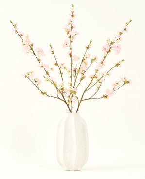 The Silk artificial flower bouquet Cherry blossom light pink 94 cm features delicate pink artificial cherry blossoms in a white ceramic vase, which adds elegance against a plain light background.