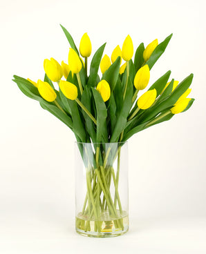The Silk artificial bouquet Tulips in vase Yellow consists of a bouquet of yellow tulips with green leaves in a clear glass vase, against a plain white background.