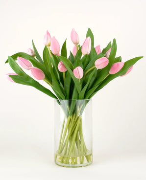 The Silk artificial bouquet Tulips in vase Pink has pink tulips with long stems and green leaves in a clear glass vase, against a plain white background.