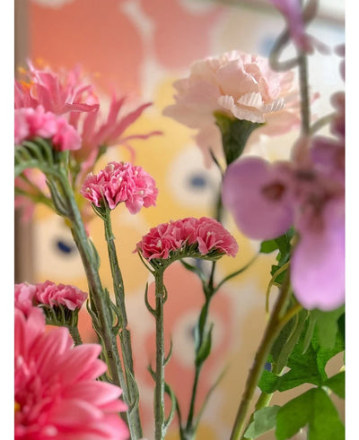 Een close-up van de Kunsttak Statice 64 cm roze kunstbloemen, met delicate roze statice-bloemen tegen een wazige, pastelkleurige achtergrond met abstracte gele en perzikkleurige vormen.