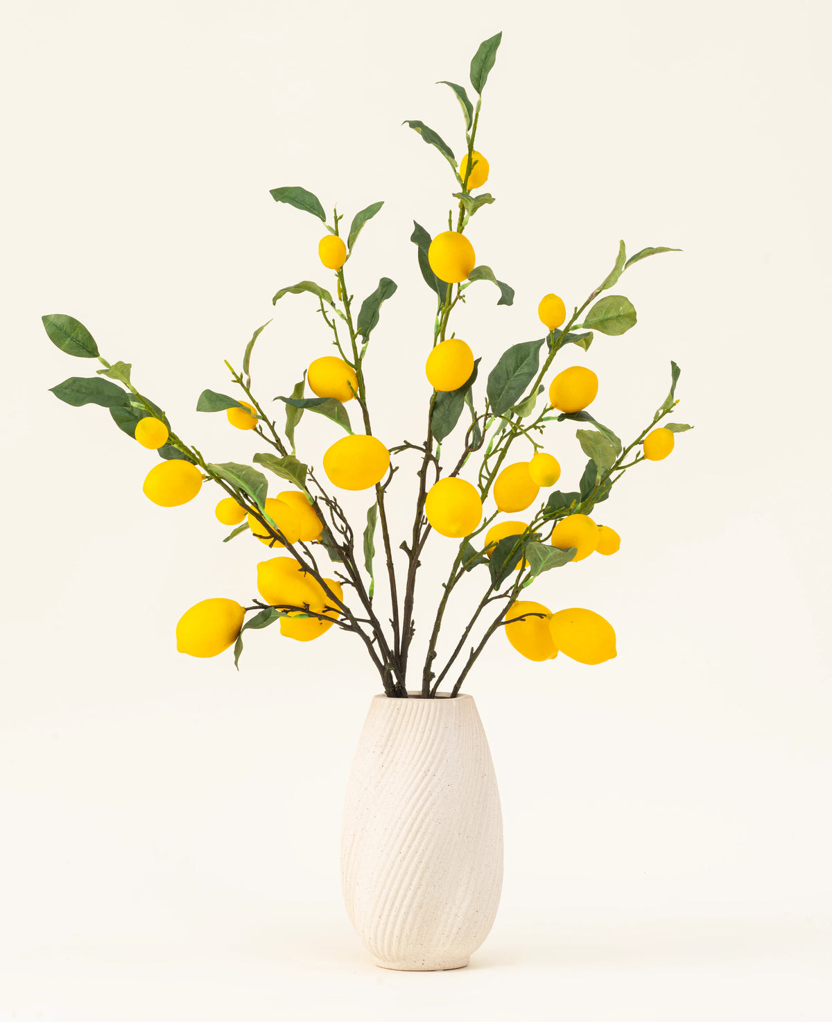 A white textured vase shows the Lemons silk artificial flower bouquet, with green leaves and vibrant yellow lemons against a light background.