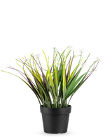 De Kunstplant Grasplant in pot UV 26 cm heeft lange groene en paarse bladeren met kleine witte bloemen, gerangschikt in een eenvoudige zwarte pot en weergegeven tegen een witte achtergrond.