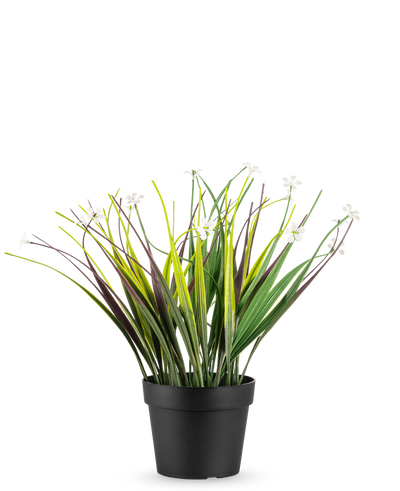 De Kunstplant Grasplant in pot UV 26 cm heeft lange groene en paarse bladeren met kleine witte bloemen, gerangschikt in een eenvoudige zwarte pot en weergegeven tegen een witte achtergrond.