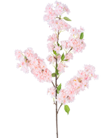 De Kunst Kersenbloesem 100 cm roze heeft een lange bruine steel, trossen lichtroze kersenbloesem bloemen en groene bladeren tegen een witte achtergrond.