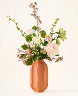 In a peach-colored ceramic vase is a bouquet of pink and white silk artificial flowers, the “Dreamy Meadow” bouquet, with green leaves and stems, against a plain, light background.