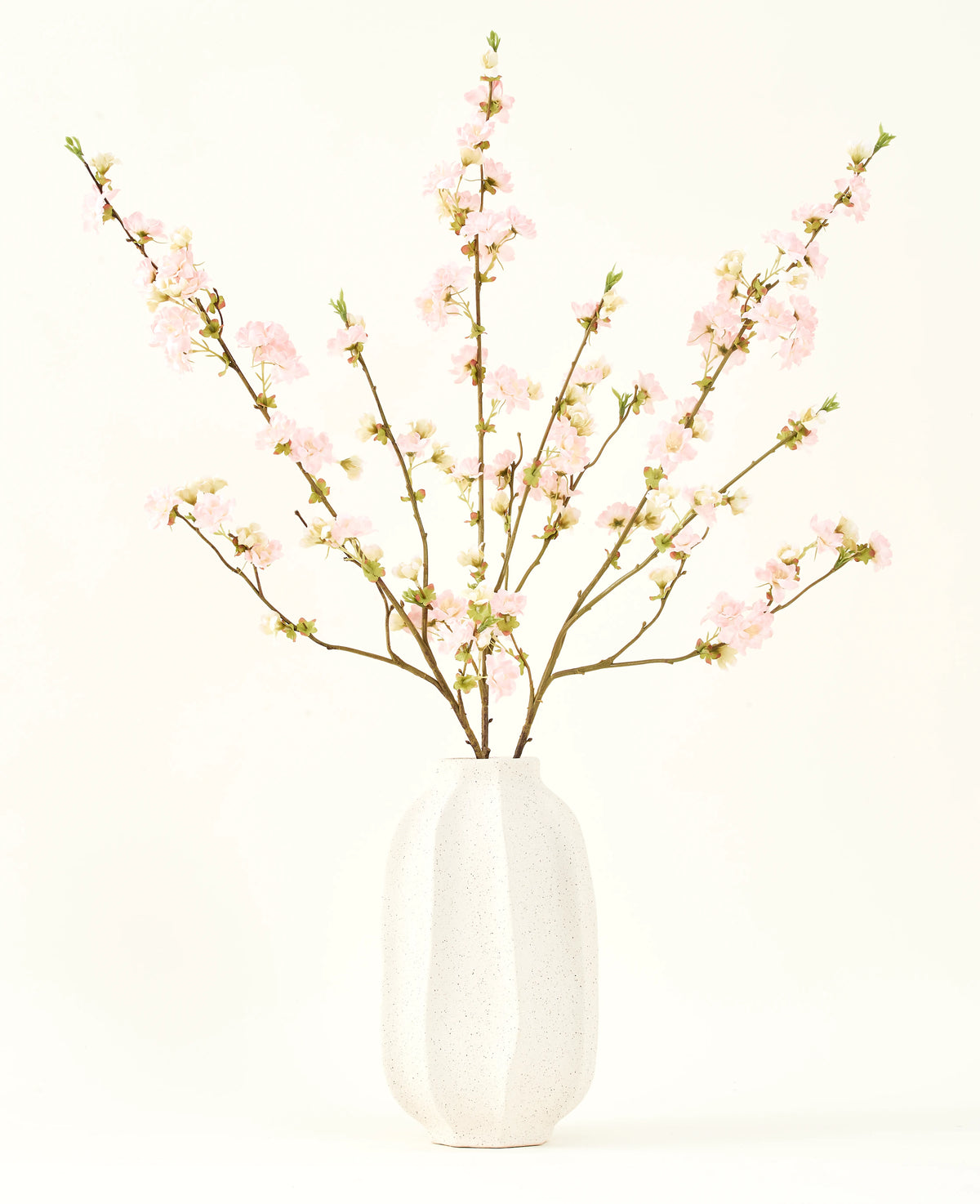The Silk artificial flower bouquet Cherry blossom light pink 94 cm features delicate pink artificial cherry blossoms in a white ceramic vase, which adds elegance against a plain light background.