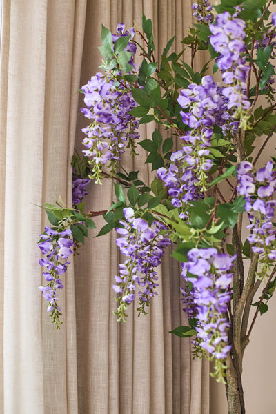 An artificial Wisteria plant of 150 cm with green leaves hangs in front of the beige curtains.