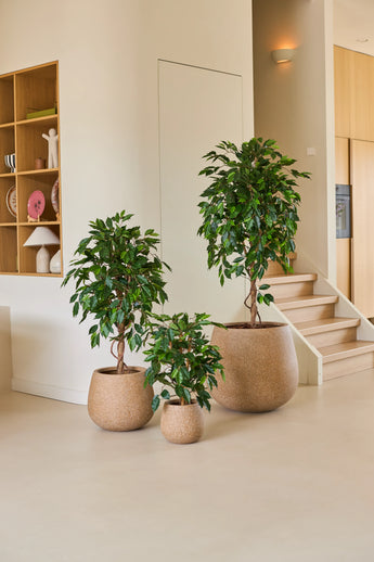 Three houseplants in pots of different sizes, including the Artificial Plant Ficus Green 90 cm, are arranged on a light-coloured floor near a staircase, with wooden shelves and home accessories in the background – an ideal arrangement of office plants for any modern workspace.