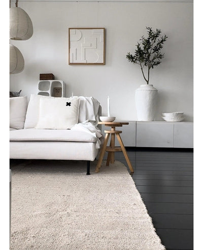 A minimalist living room with a light-colored sofa, neutral rug, white sideboard, Artificial Olive Tree 120 cm as a decorative element, abstract wall art and wooden stools - all in a soft Mediterranean atmosphere with neutral tones.