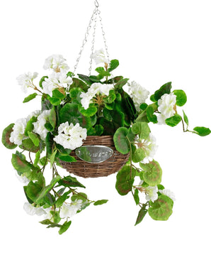 De Kunst begonia Wit in Mand UV 70cm is een hangende rieten mand met groene bladeren en witte begonia bloemen, opgehangen aan zilveren kettingen tegen een witte achtergrond.