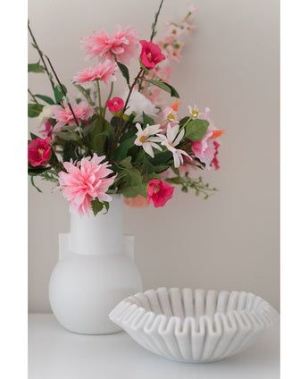 Een witte vaas met een Kunstbloem Rododendron Azalea 73 cm fuchsia staat naast een witte schaal van geribbeld keramiek op een effen ondergrond tegen een neutrale achtergrond.