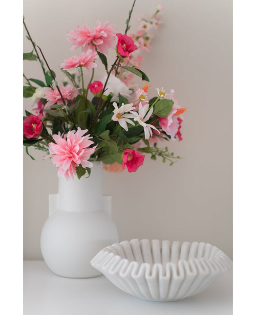 A white vase with an Artificial flower Rhododendron Azalea 73 cm fuchsia stands next to a white bowl of ribbed ceramic on a plain surface against a neutral background.