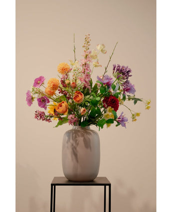 The Artificial Dogwood Real Touch Light Yellow 74cm, a lifelike light yellow artificial flower, stands in a ceramic vase with green foliage on a black metal stand against a plain beige background.