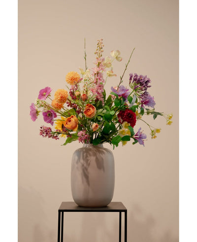 The Artificial Dogwood Real Touch Light Yellow 74cm, a lifelike light yellow artificial flower, stands in a ceramic vase with green foliage on a black metal stand against a plain beige background.