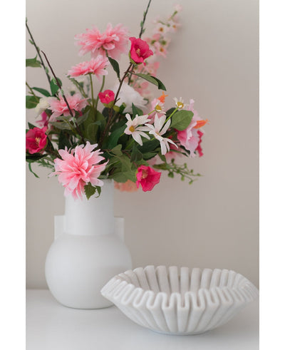 Een Kunstbloem Dahlia 68 cm roze in een witte vaas staat naast een schaal van wit keramiek met ruches op een wit oppervlak, tegen een effen lichte achtergrond.
