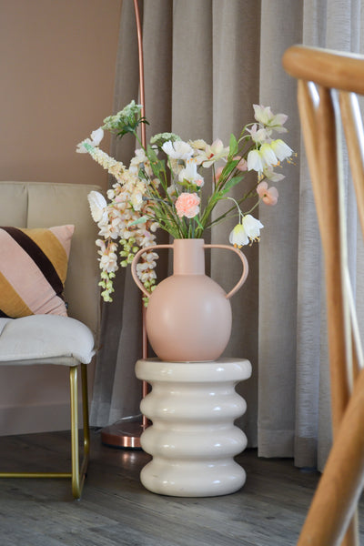 The Artificial Flower Fritillary 94 cm white stands in a light pink ceramic vase with handles, placed on a wavy white base next to a modern chair with a striped cushion and neutral curtains in a stylish room.