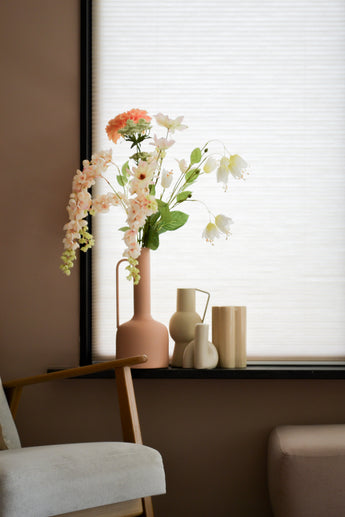 A pastel living room corner with a wooden chair, a soft footstool and a windowsill with the Artificial Flower Fritillary 94 cm white artificial flower in a pink vase next to minimalist ceramic decor against white blinds.