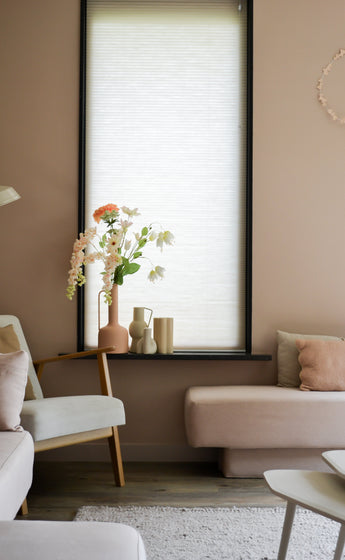 A cozy living room with light pink walls, a large window with a white roller blind, cream and blush sofas and a wooden chair with the Artificial Flower Fritillary 94 cm white next to decorative objects on the windowsill.