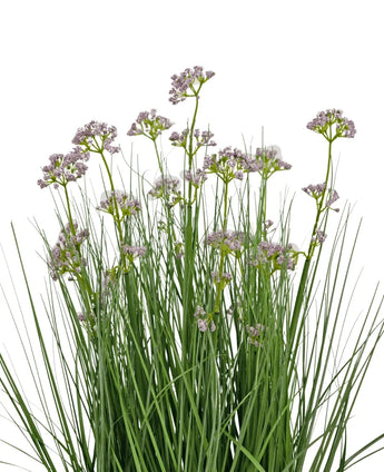 The Artificial Grass Leek Flower Onion Grass Pot 60cm has high, thin green leaves and bunches of small, delicate light purple flowers on long stems. The arrangement is fire retardant and depicted against a white background.