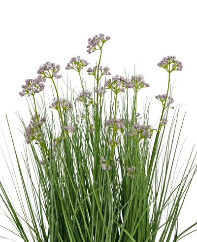 De Kunstgras Prei Bloem Ui Graspot 60cm heeft hoge, dunne groene bladeren en trossen kleine, delicate lichtpaarse bloemen op lange stelen. Het arrangement is brandvertragend en afgebeeld tegen een witte achtergrond.