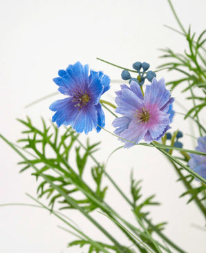 De Kunstgras paarse Gesang Bloem uiengraspot (56cm, brandvertragend) heeft delicate paarse bloemen met groene varenachtige bladeren en kleine ronde knoppen, tegen een effen witte achtergrond.