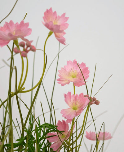 De Kunstgras roze Gesang Bloem uiengraspot 56cm brandvertragend heeft delicate roze bloemen met slanke groene stelen en smalle bladeren, gerangschikt tegen een lichte achtergrond voor een zacht, luchtig effect.