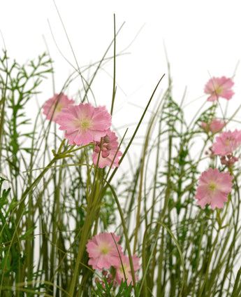 De Kunstgras roze Gesang Bloem uiengraspot 90cm brandvertragend heeft roze bloemen met een lichtgroen hart die bloeien tussen hoog, dun gras en weelderige bladplanten, allemaal tegen een witte achtergrond.