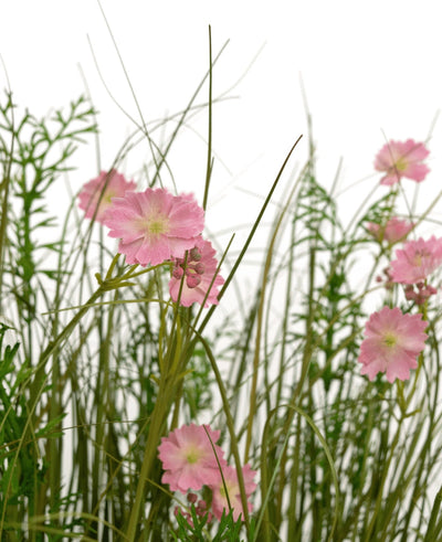 De Kunstgras roze Gesang Bloem uiengraspot 90cm brandvertragend heeft roze bloemen met een lichtgroen hart die bloeien tussen hoog, dun gras en weelderige bladplanten, allemaal tegen een witte achtergrond.