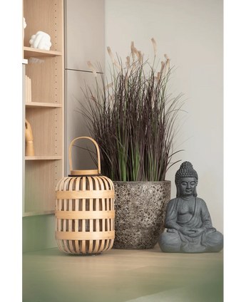 A wooden lantern, a tall stone pot with 100 cm artificial onion grass bonsai (fire retardant) and a gray Buddha statue are arranged on a light-colored surface, near a wooden shelf and a pale wall.