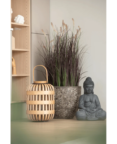 A wooden lantern, a tall stone pot with 100 cm artificial onion grass bonsai (fire retardant) and a gray Buddha statue are arranged on a light-colored surface, near a wooden shelf and a pale wall.
