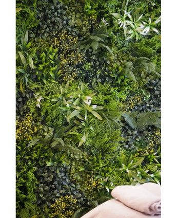 A lush, textured backdrop is created by the Kunsthaag Freshness 100x100 cm UV vertical garden wall, densely covered with green foliage. Two folded beige towels are visible at the bottom right.
