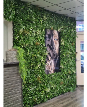 A 100x100cm Kunsthaag Savanne fire retardant panel with lush greenery surrounds a large black and white facial portrait in an interior space with tiled ceiling panels and a small counter to the left.