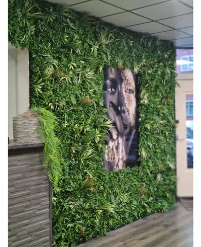 A 100x100cm Kunsthaag Savanne fire retardant panel with lush greenery surrounds a large black and white facial portrait in an interior space with tiled ceiling panels and a small counter to the left.