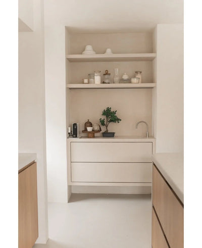 Minimalist kitchen corner with light wooden shelves with pots, vases, decor, a countertop with small appliances and the Artificial Bonsai Juniper 40 cm potted plant, plus built-in drawers and a small tap - all in neutral tones.